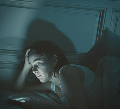 Женщина смотрит в телефон ночью на кровати